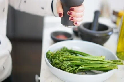 broccolini in a bowl with fresh black peppercorns being ground onto it