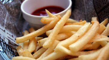 closeup of french fries in a basket with ketchup in a white sauce bowl