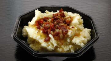 Closeup of mashed potatoes topped with bacon bits in a bowl with a dark background