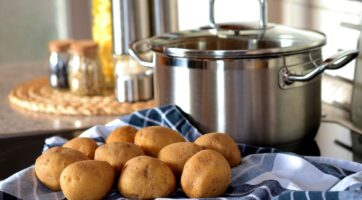 closeup of potatoes in kitchen on blue checkered towel, in front of silver, shiny pot with a lid