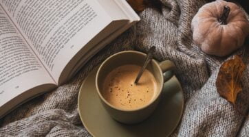 picture of pumpkin coffee in a mug next to a book on a blanket
