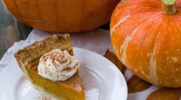 picture of a slice of pumpkin pie with whipped cream on top and pumpkins in the background