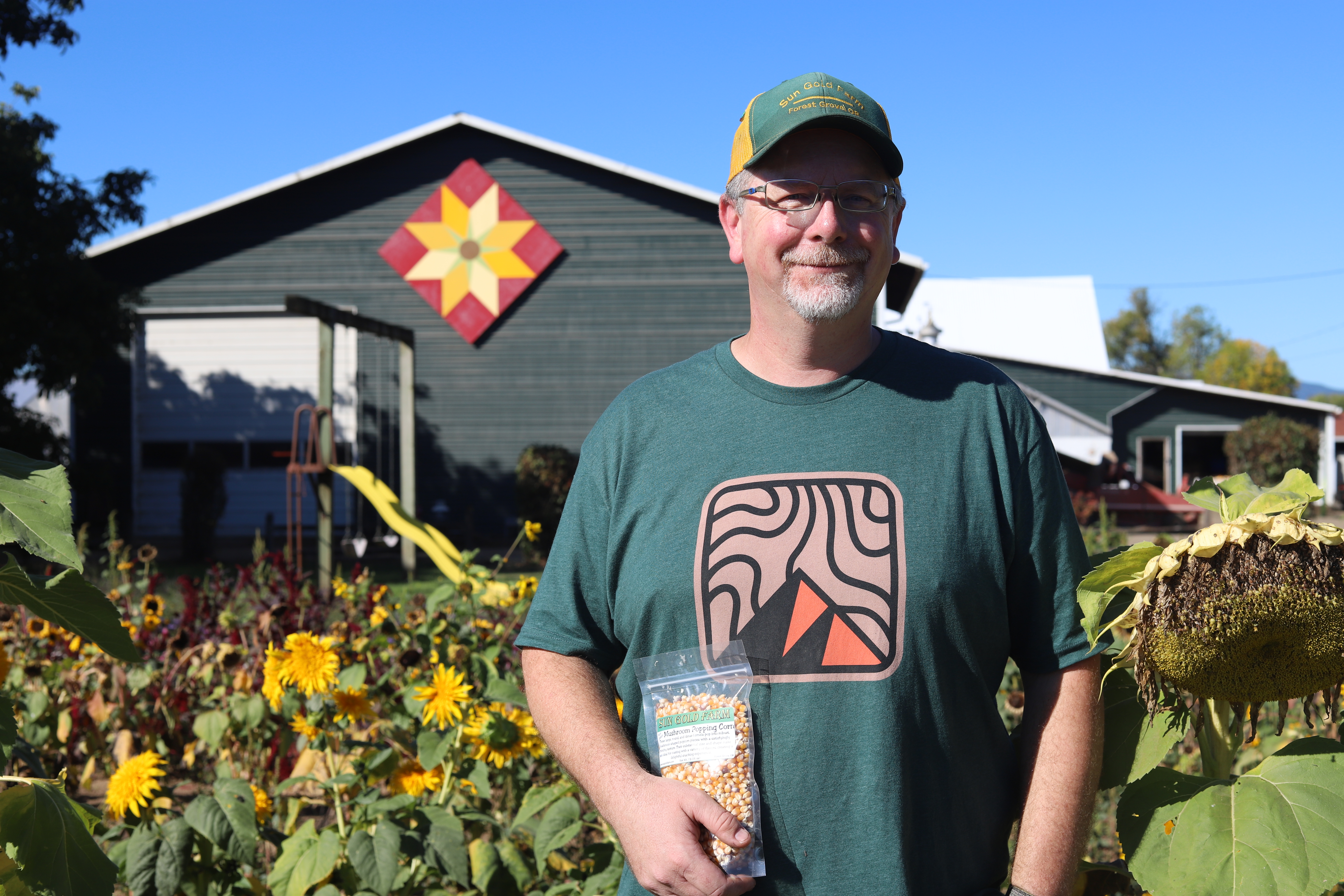 A man stands in front of a barn holding a bag of popcorn kernels